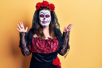 Young woman wearing day of the dead costume over yellow celebrating mad and crazy for success with arms raised and closed eyes screaming excited. winner concept