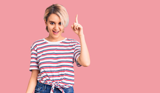 Young beautiful blonde woman wearing casual clothes pointing finger up with successful idea. exited and happy. number one.