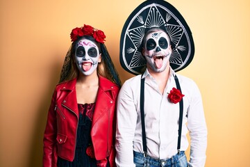 Couple wearing day of the dead costume over yellow sticking tongue out happy with funny expression....