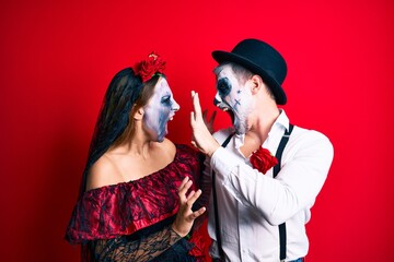 Beautiful couple wearing day of the dead costume over isolated red background.