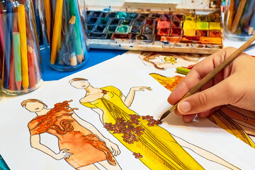 Fashion designer at work. He comes up with a new dress for the girl. Drawing with watercolors on...
