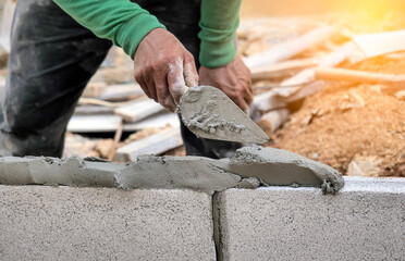 Close up of a worker putting cement into the brick wall at construction site - obrazy, fototapety, plakaty