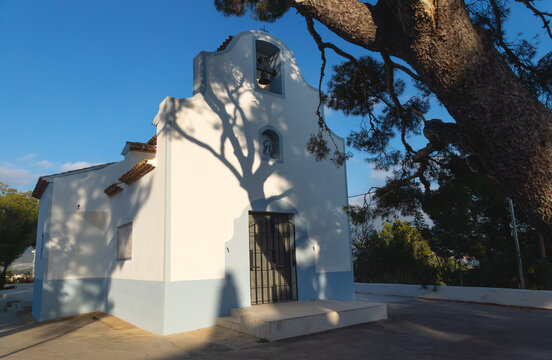 White chapel 'Ermita de Sant Vicent' sunlit with shadows from big tree in La Nucia, Costa Blanca, Spain
