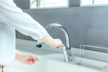 Fototapeta premium 爽やかな白いキッチンで女性が手を洗おうとしている