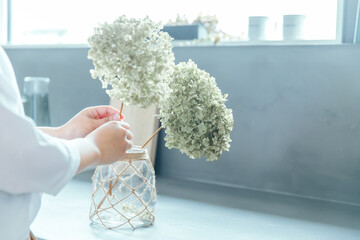 明るい白い部屋の窓辺で花瓶に花を飾っている　flower room interior