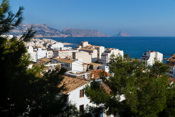 Obraz premium View over the white washed houses between fir trees with acient roofs to the ocean and the rock of Calpe, Altea, Costa Blanca, Spain