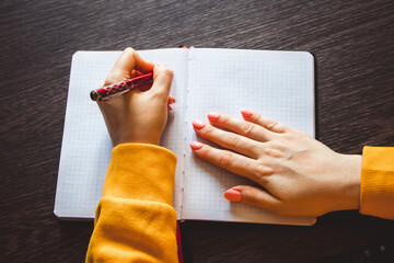 Young woman holds a pen in her left hand and writes  note in blank notebook. International...