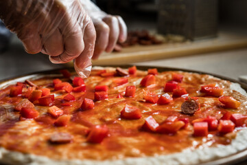 Hand Choosing Fresh Ingredients and Chef Preparing a Pizza Pie with Red Peppers in a Kitchen