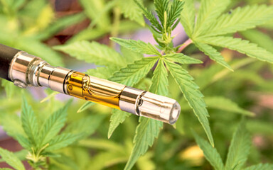 oil filled vape pen cartridge up-close against green cannabis leaf background