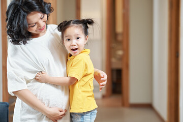 Happy excited little girl hugging her pregnant mother and looking at camera