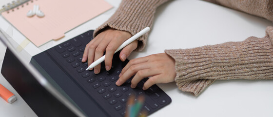 Female typing on tablet keyboard while holding stylus pen on office desk