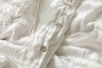 Trendy organic natural linen bedclothes with wooden buttons closeup. Bedding, morning light,...