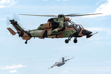 Armed reconnaissance helicopter hovering while a military cargo aircraft departs in the background.