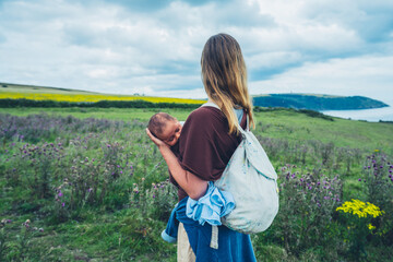 Young mother with baby in sling by the seaside