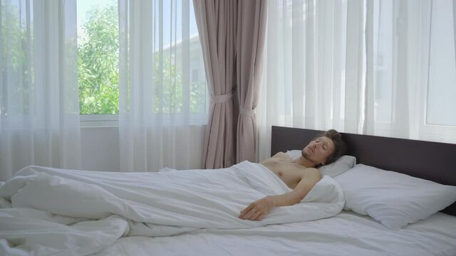 A young man in a bed feels that it's very hot. Eventually he turns on an air conditioner