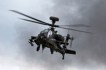 Army attack helicopter flying past dark smoke plumes.