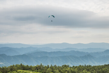 龍門山頂から稜線の上を飛ぶパラグライダーを空撮