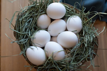 Bowl with hay and white eggs on a wooden table.