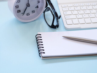 Blue workplace desk table with a notebook and pen, eyesglass, keyboard, clock at 7:00 am. Business and education concept. Space for text..