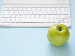 Close up green apple and keyboard on blue workplace desk table. Business and education concept. Space for text..