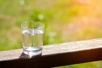Water glass stands on wooden plank on sunbeams. Hydration at hot summer days concept. Healthy lifestyle symbol. Healthy water drink sunny