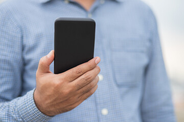 Close up male hands holding using black smartphone on city background.