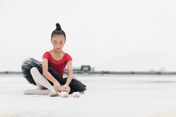 Asian ballerina girl tying pointe shoelace before practicing the ballet dancing sitting on rooftop...