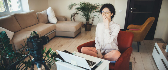 Yawning caucasian woman with black hair using a laptop at home before having online lessons