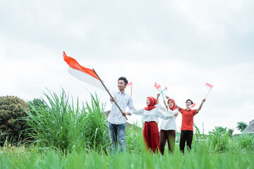 asian young man in white walking carrying an Indonesian flag with stick and three of his friends walk behind him with a small flags