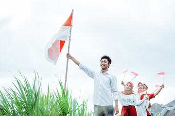 a boy in white carrying raise an Indonesian flag with stick and three of his friends behind follow him with a small flags