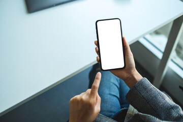 Top view mockup image of a woman holding and pointing finger at a mobile phone with blank white desktop screen