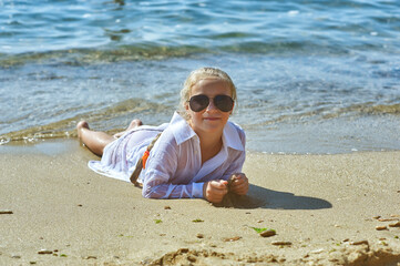 A little girl is resting at a seaside resort . A happy child in a white shirt takes a sun bath on the sea