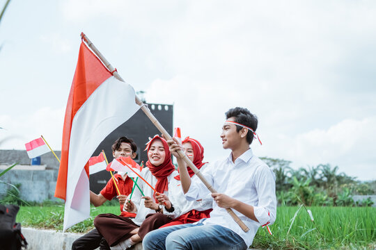 Young Man Sit Carrying Stick With Indonesian Flag And Three Of His Friends Sit Beside Him With Many Small Flags At The Rice Field