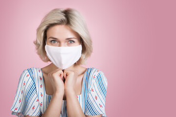 Charming caucasian woman with blonde hair and medical mask on face posing on a pink wall with free space