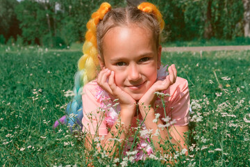 beautiful girl's portrait. girl laying on a grass with white flowers.a girl wearing kanekalon braids. colorful braids ona kid's hair. festive hairdo.