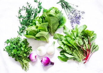Fresh aromatic garden herbs and vegetables on a white background, top view. Spinach, coriander,...