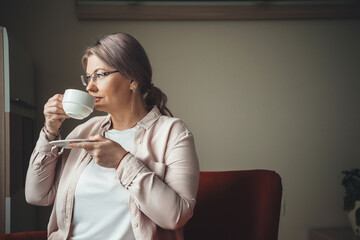 Pensive caucasian woman with blonde hair drinking a coffee near the window