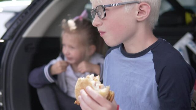 A boy with an appetite eats a cheeseburger in a car at a stop during a family car journey.