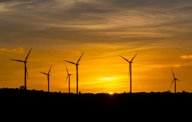 Fototapeta premium Silhouette wind turbine with twilight sky and sunlight ray for clean energy plant on the mountain.