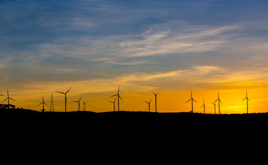 Silhouette wind turbine with twilight sky and sunlight ray for clean energy plant on the mountain.
