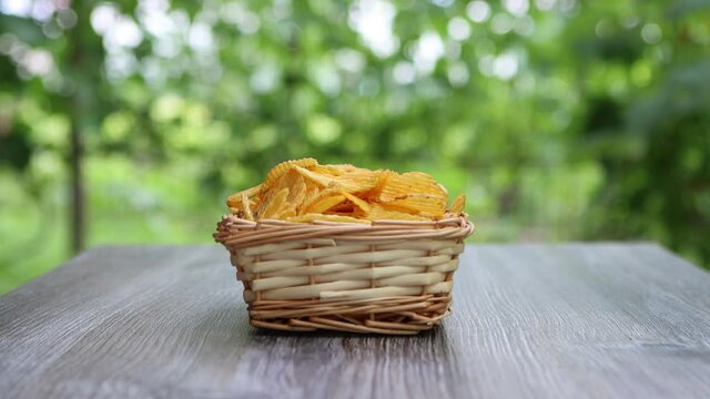 hand of adult female taking potato chips from wickered bowl in garden
