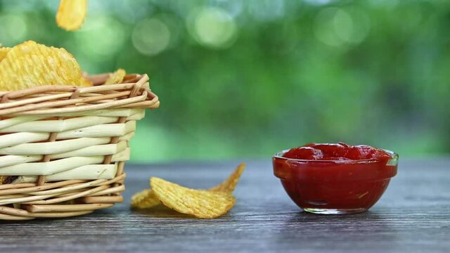 hands of adult female taking potato chips from wickered bowl and dipping them in ketchup slow motion
