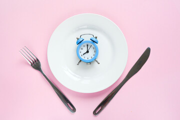 Blue alarm clock, fork, knife and empty plate on pink background. Intermittent fasting concept- Image. Time concept. Breakfast concepte. 8 a.m.