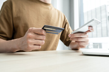 The businessman's hand is holding a credit card and using a smartphone for online shopping and internet payment in the office