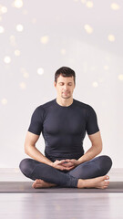 Man sitting at lotus yoga pose. Home morning routine. Teacher fitness studio. Asana class. Online exercise. Relaxation indoor. Male prayer in house room. Light background. Vertical. Close eyes