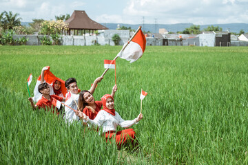 having fun together of young people march on the rice field hold indonesian flag with attributes to commemorate independence day