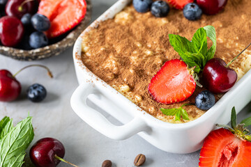 Classic Italian dessert Tiramisu decorated with strawberries, cherries and mint on a white background.