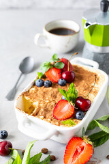 Classic Italian dessert Tiramisu decorated with strawberries, cherries and mint on a white background.