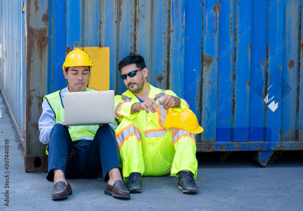 Poster two foreman workers use a laptop computer sitting near the container box at container cargo.
