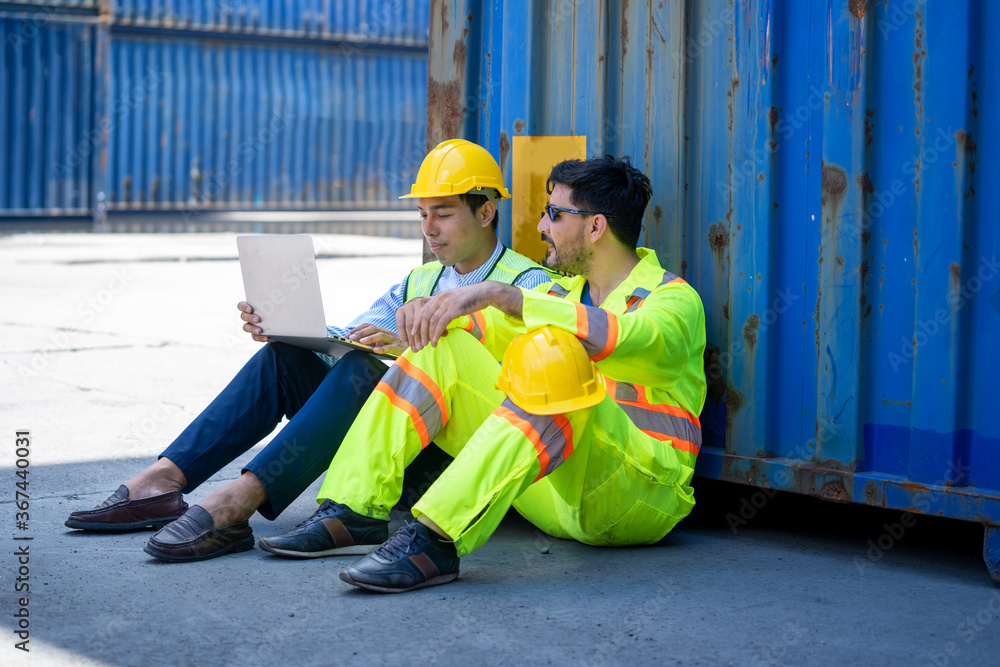 Poster two foreman workers use a laptop computer sitting near the container box at container cargo.